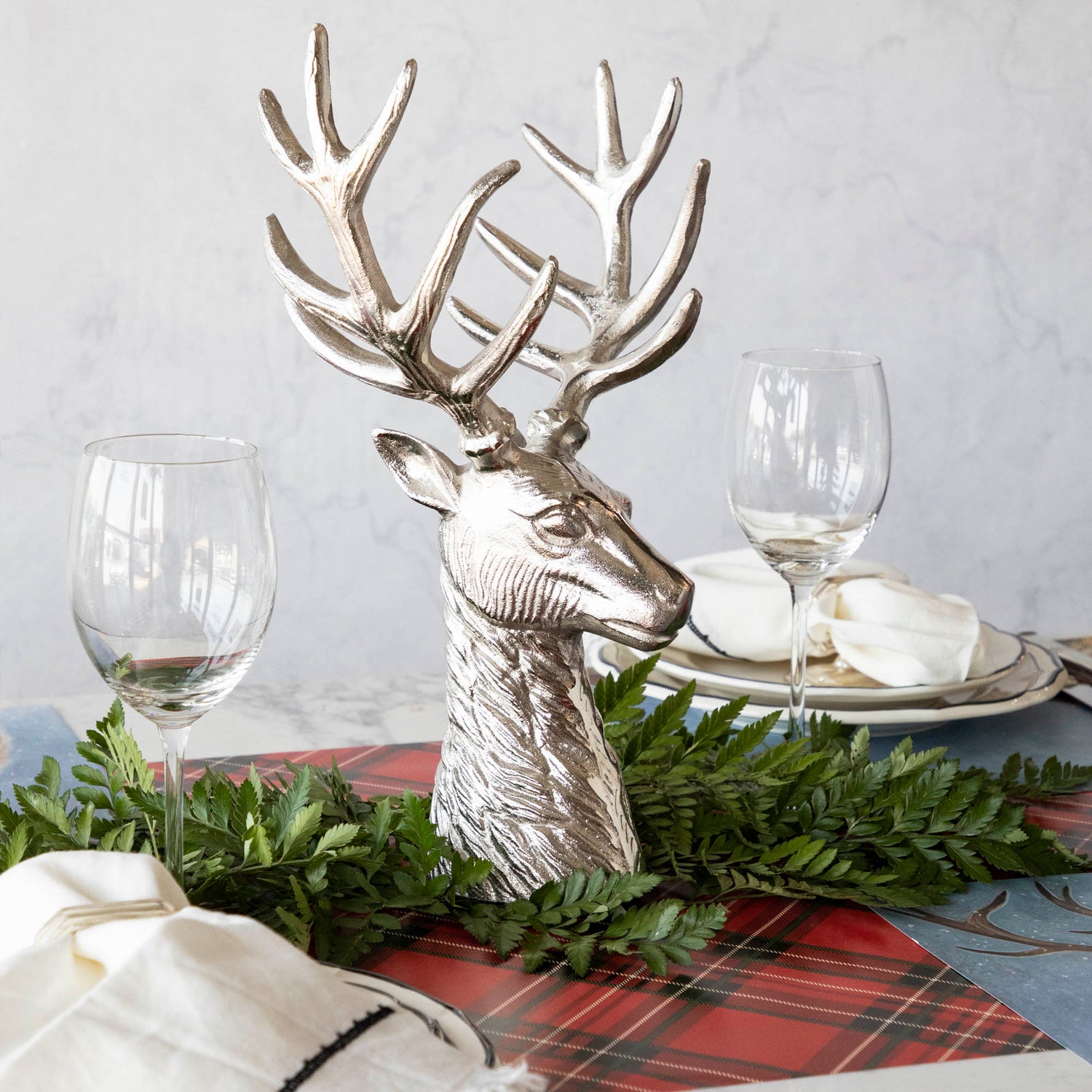 An aluminum Reindeer Bust, in the center of a woodland themed table setting, surrounded by a leaf garland.