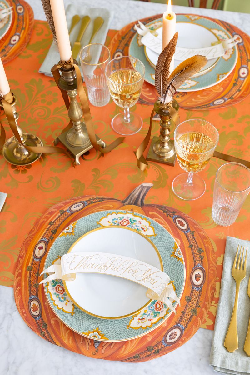 Thanksgiving-themed table setting with decorative plates, glasses, and cutlery on a patterned tablecloth.