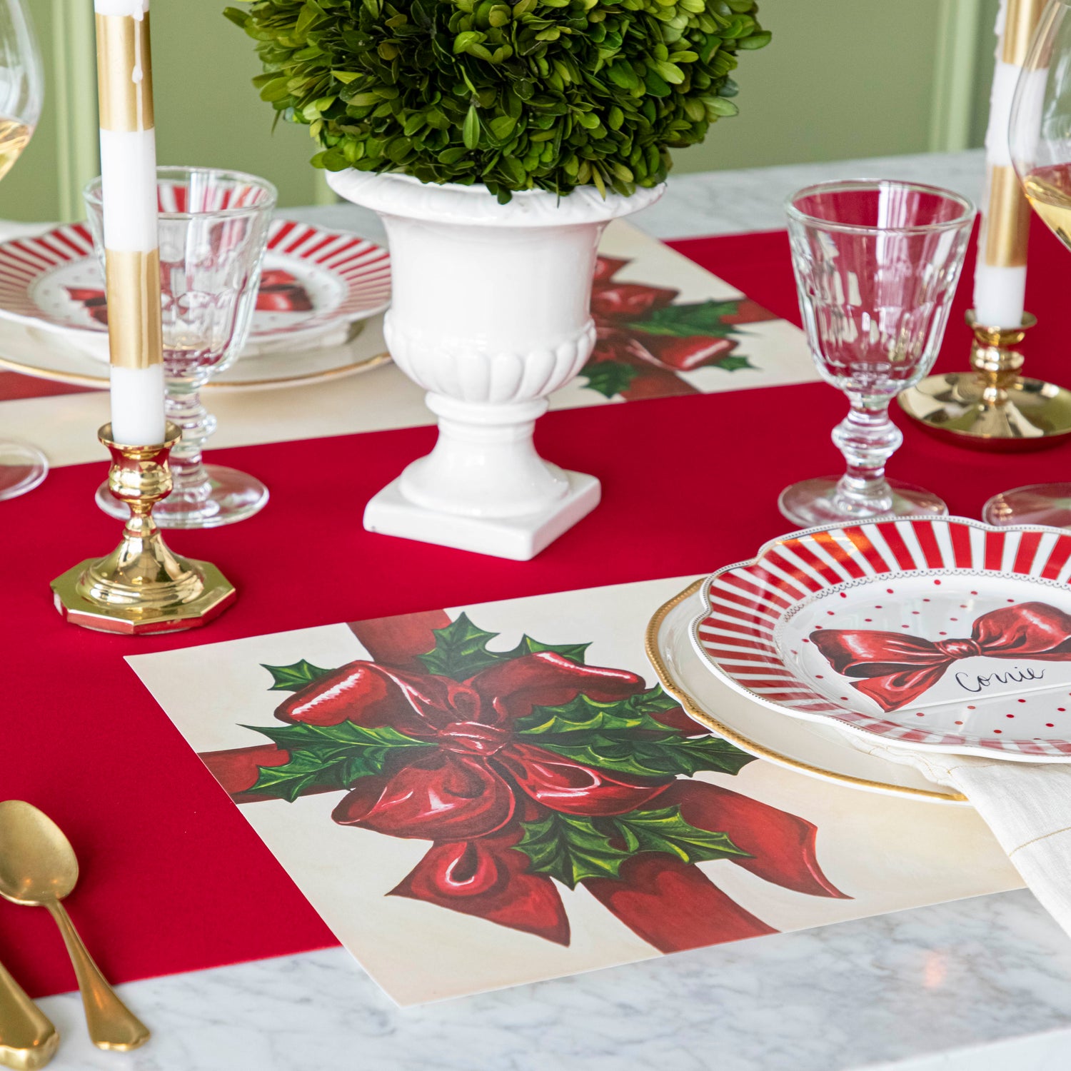 An elegant Christmas themed table setting with the Red Flocked Runner underneath the Christmas Present Placemat and an urn with a boxwood ball as the centerpiece.