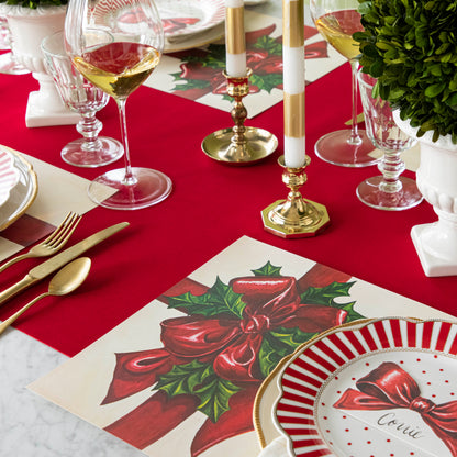 An elegant, Christmas themed table setting with the Red Flocked Runner underneath the Christmas Present Placemat and Bow Place Card resting on a plate. 