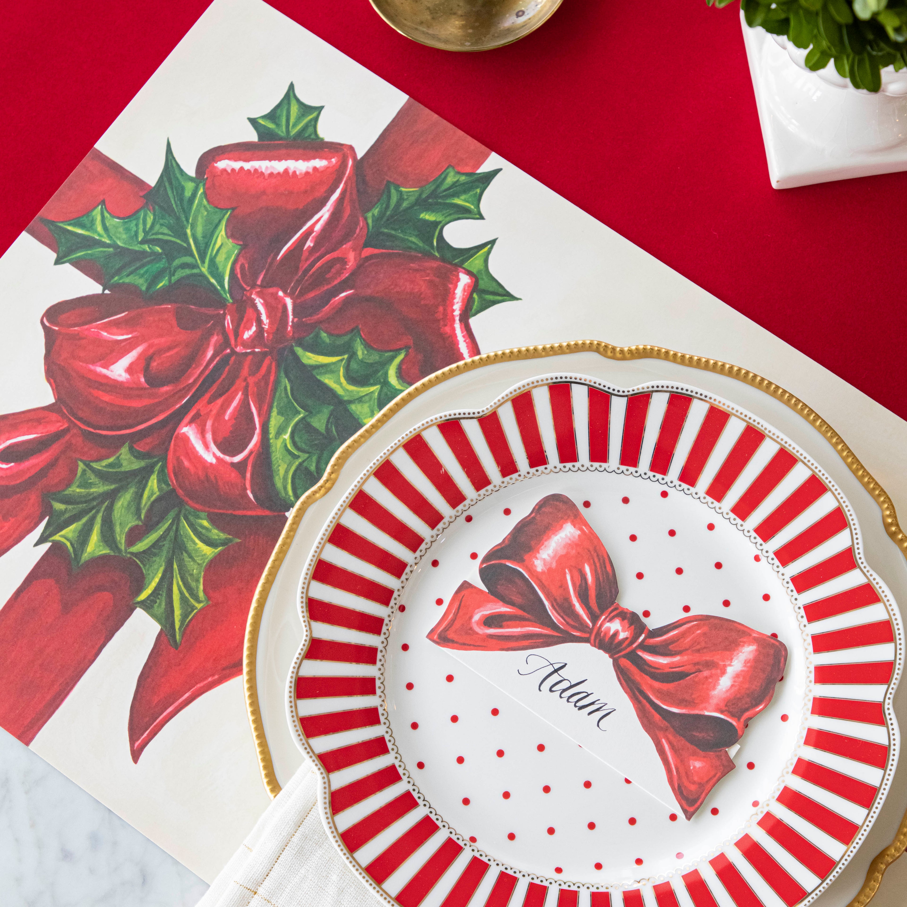 An elegant, Christmas themed table setting with the Red Flocked Runner underneath the Christmas Present Placemat and Bow Place Card resting on a plate. 