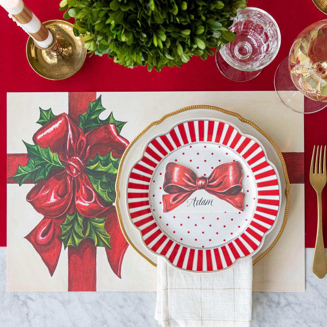 An elegant, Christmas themed table setting with the Red Flocked Runner underneath the Christmas Present Placemat and Bow Place Card resting on a plate. 