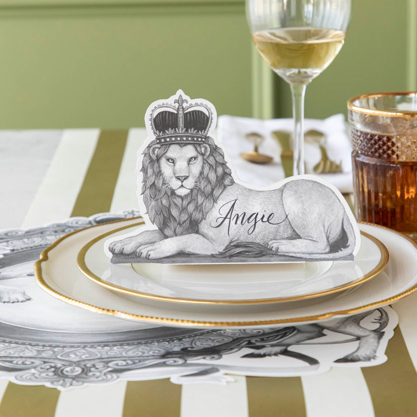 Regal Lion Place Card with &quot;Angie&quot; written on it, sitting upwards on dinner plates.