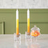Two taper candles with a yellow, orange, and white color gradient design, resembling candy corn, displayed in front of a green wall.