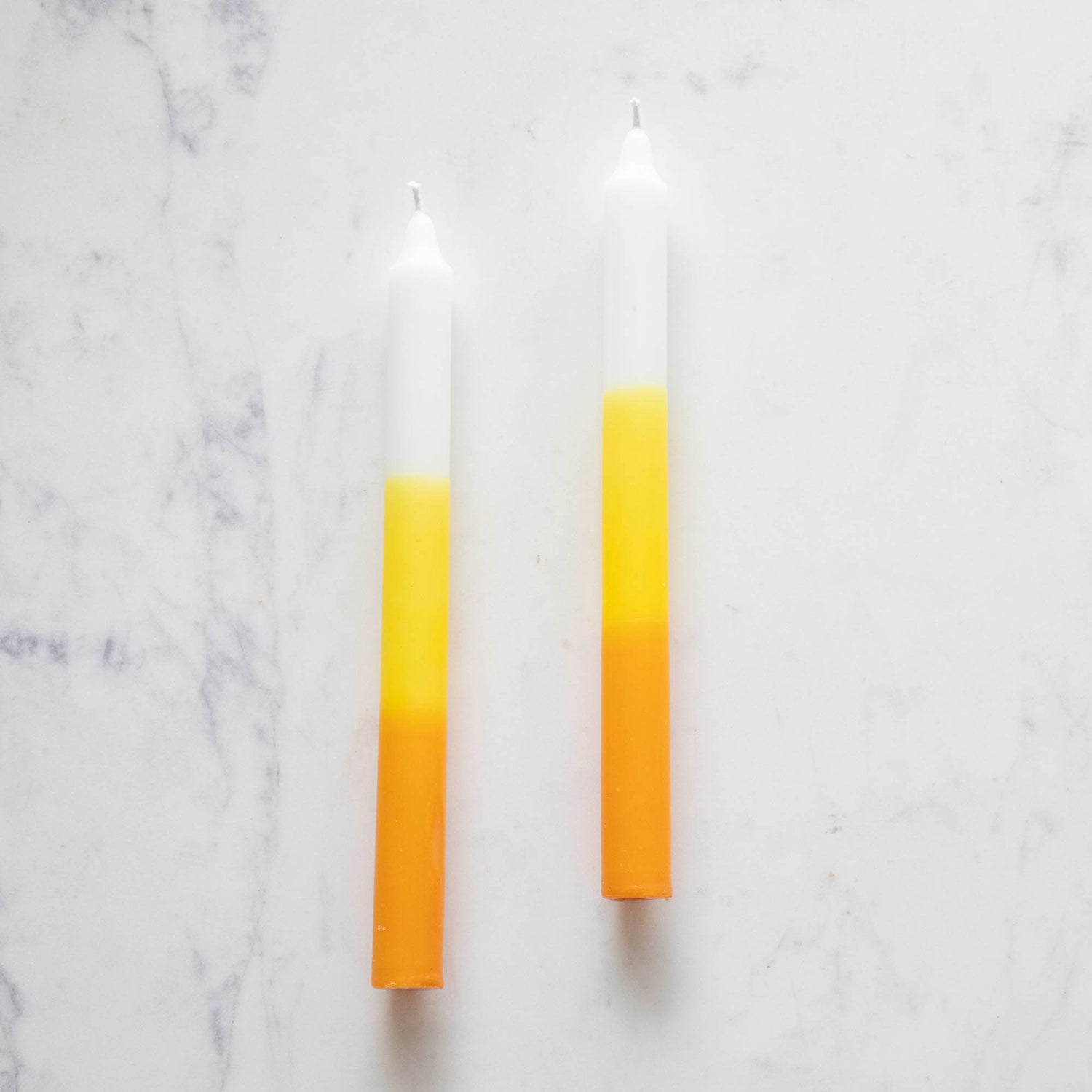 Two taper candles with a yellow, orange, and white color gradient design, resembling candy corn. 