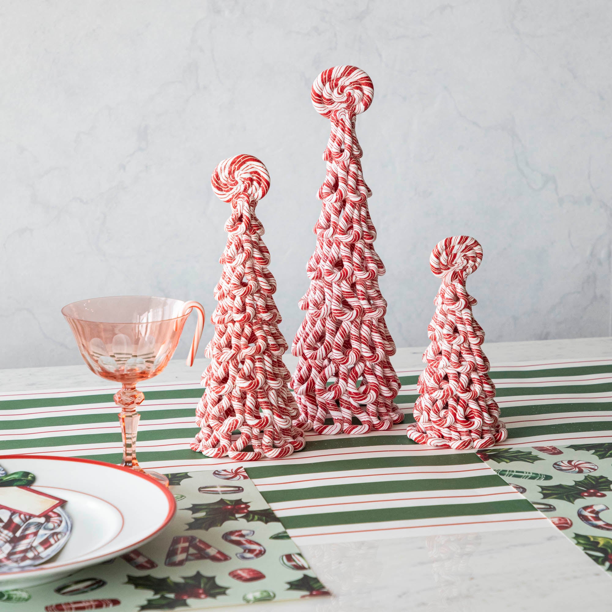 Three assorted sizes of peppermint trees on a table with peppermint themed holiday table setting.