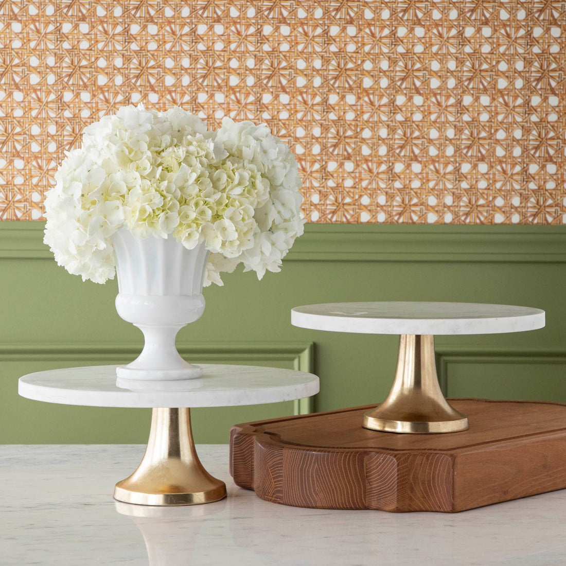 A bouquet of white hydrangeas in a white vase on a Bidk Home Marble Cake Plate with Antique Brass Base with decorative tables and a textured background.
