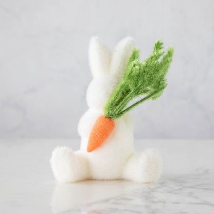 A Glitterville Flocked Bunny with Carrot holding a carrot on a table.