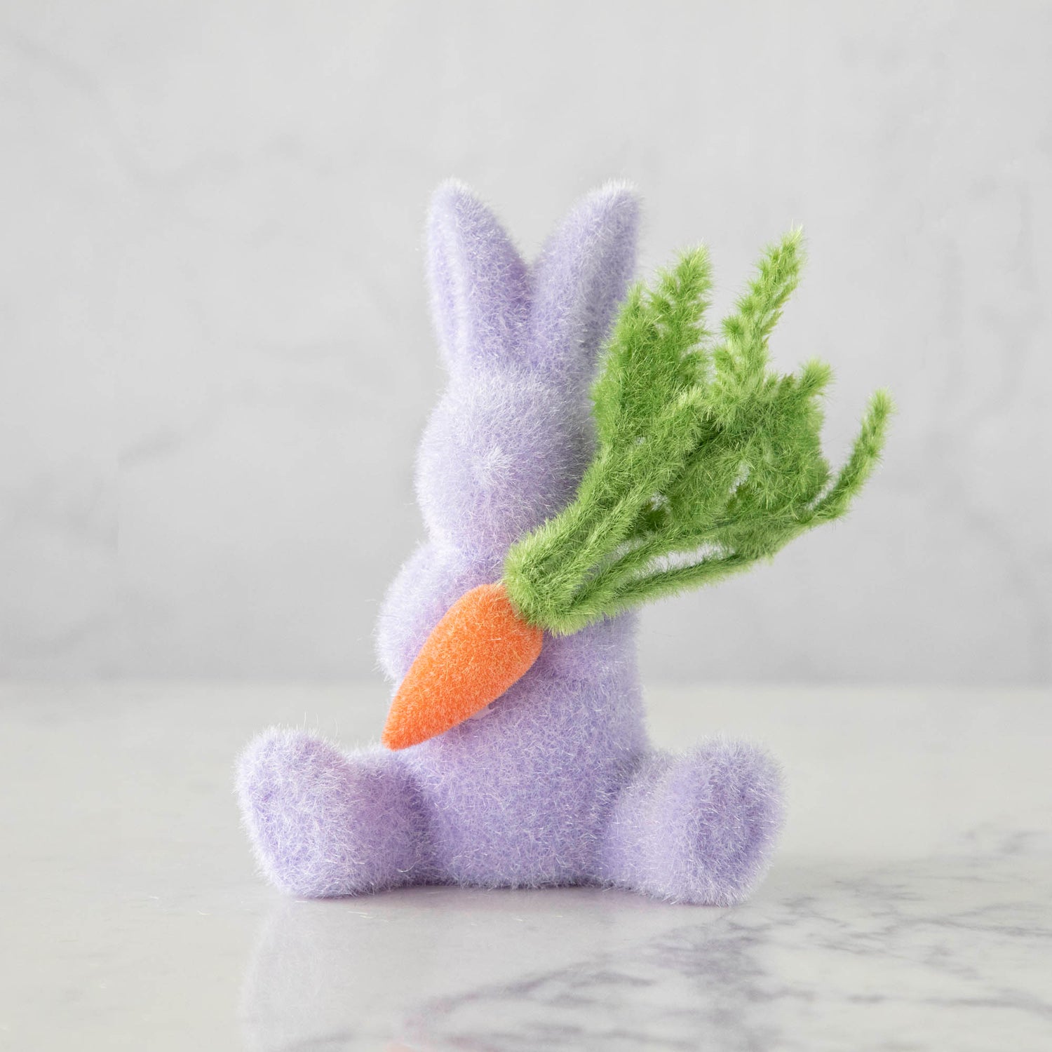 A Glitterville flocked bunny holding a carrot on a table, representing Easter and the arrival of spring.