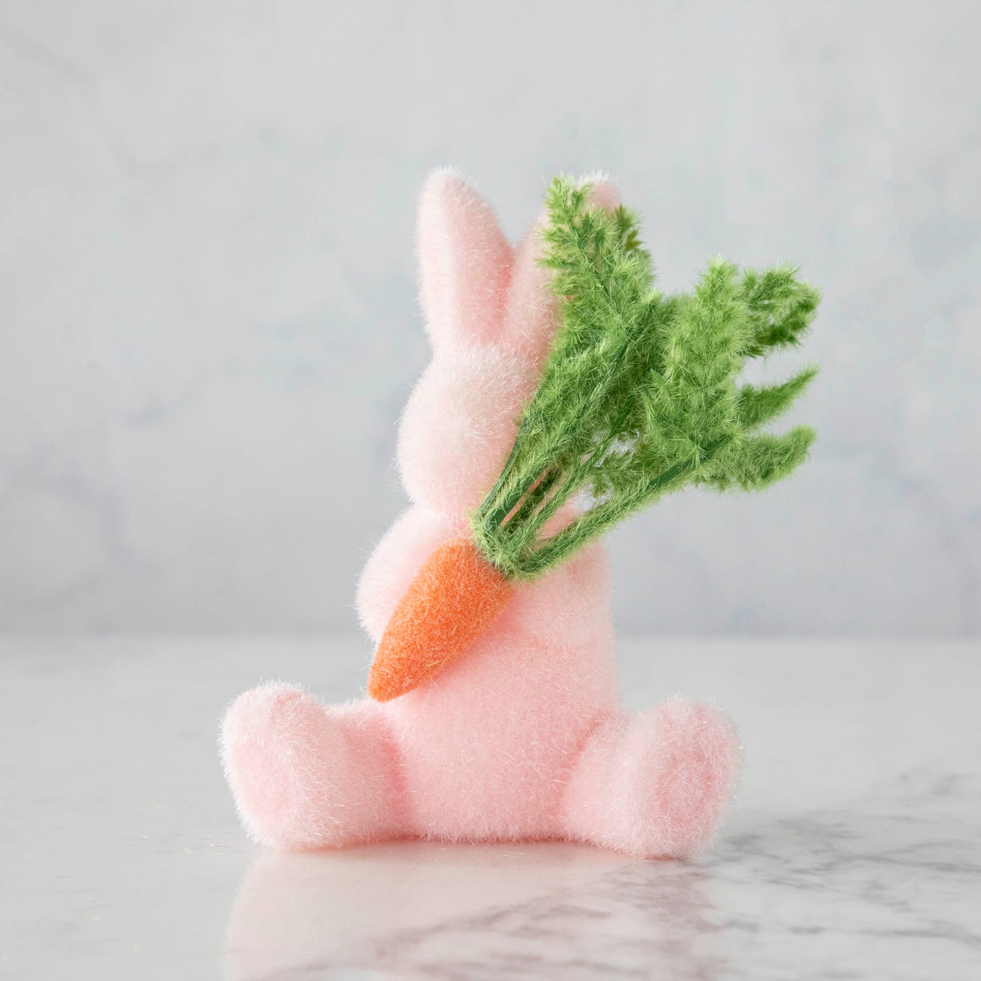 A Glitterville flocked pink bunny holding a bunch of carrots, perfect for Easter.