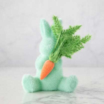 A spring-themed Glitterville flocked bunny holding a carrot on a marble table.