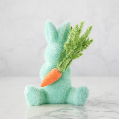 A Glitterville flocked blue bunny holding a carrot on a marble table.