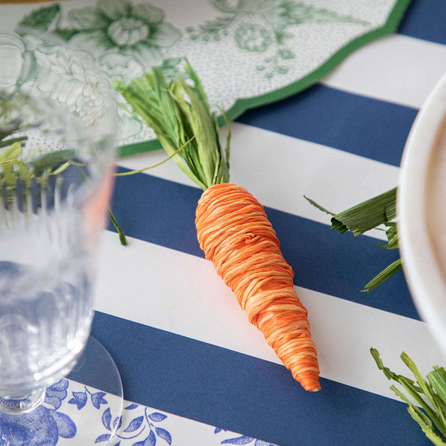 A Glitterville Easter basket filled with Natural Carrots sits on a blue and white striped tablecloth.