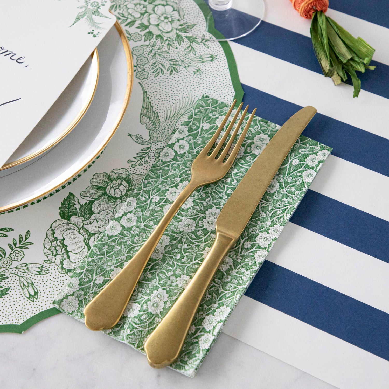 A table setting with a gold fork and knife on a Green Calico Napkins, Hester &amp; Cook striped tablecloth.
