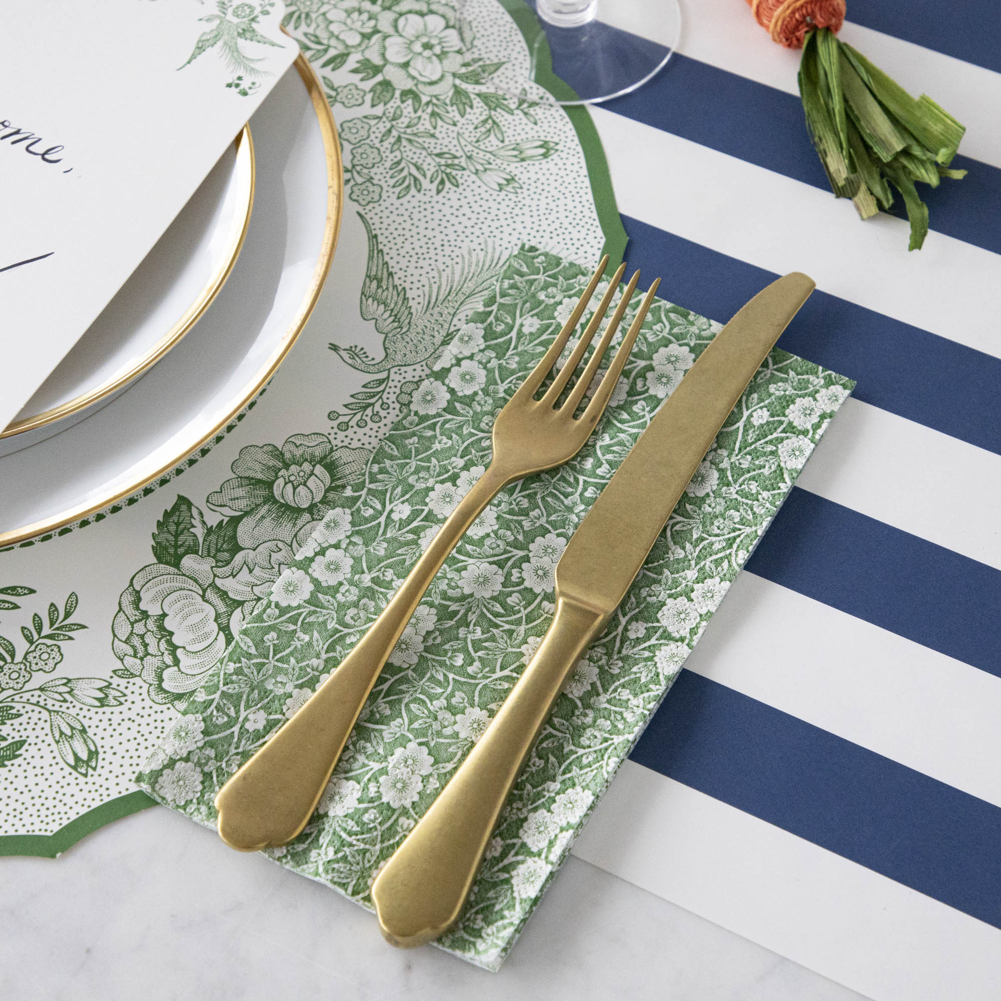 A table setting with a gold fork and knife on a Green Calico Napkins, Hester &amp; Cook striped tablecloth.