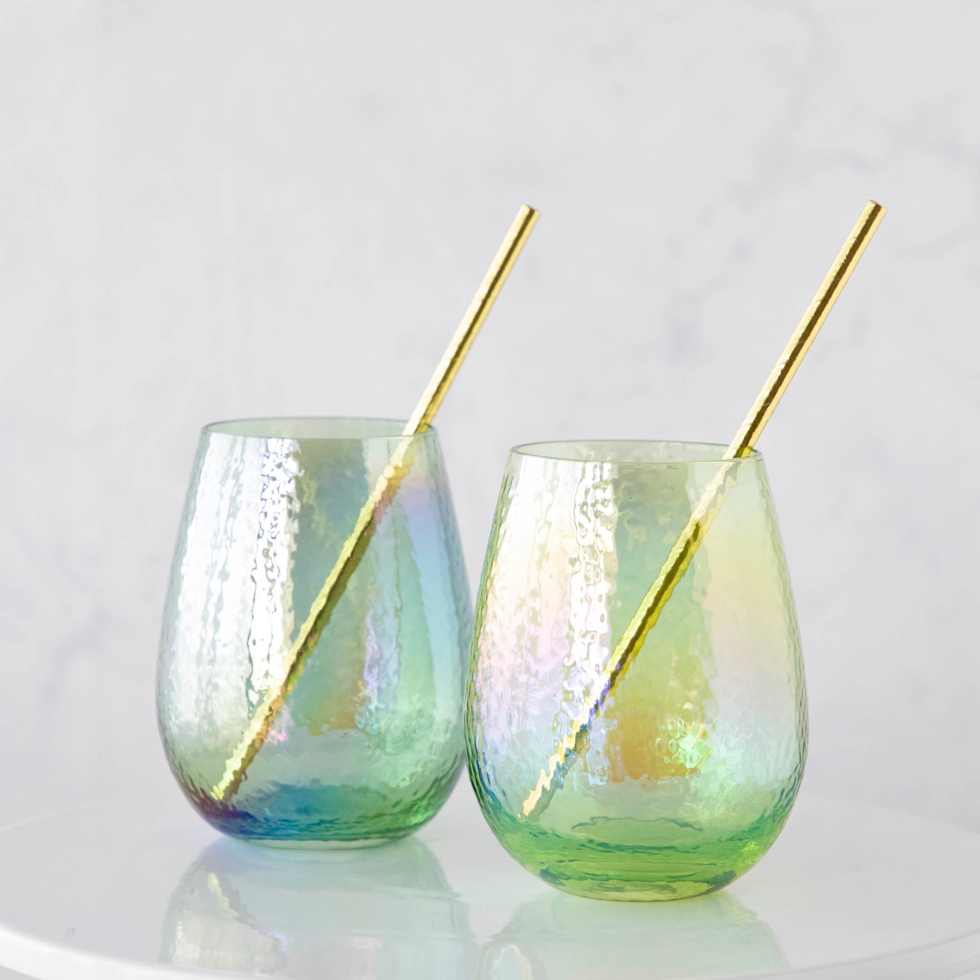 Two Luster Stemless Glasses with gold straws sitting on a white table in a cozy home, ready to serve your favorite drink.
