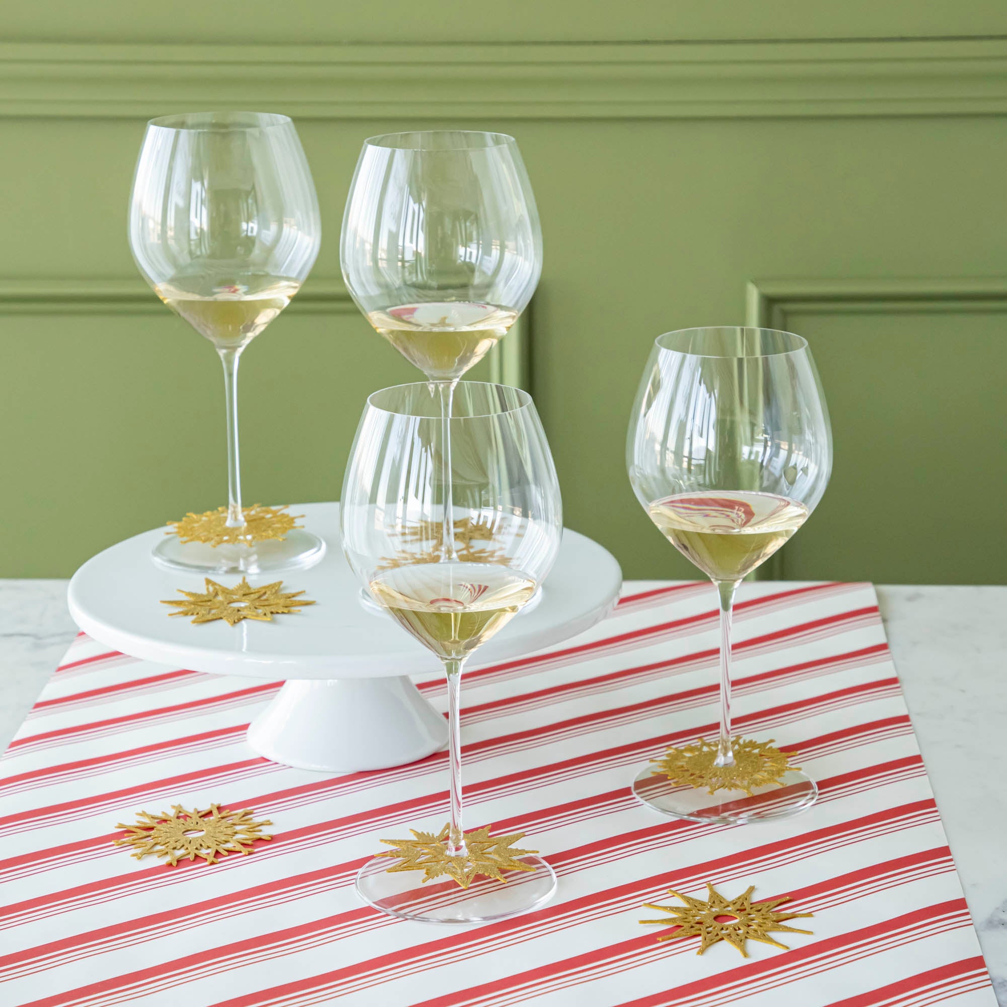 Four wine glasses with a Stemware Snowflake Collar around the base and scattered collars on the Peppermint Stripe Runner.