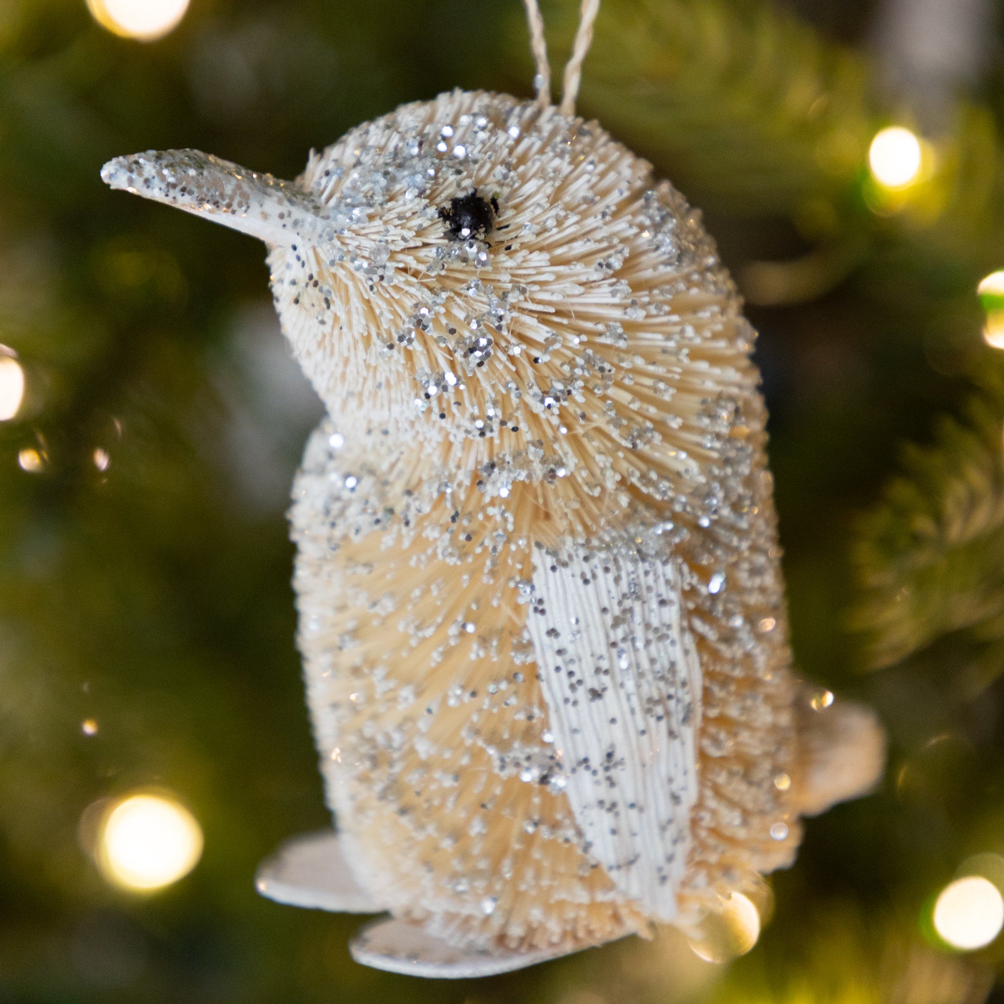 Decorative penguin ornament with glittery texture on a blurred Christmas tree background.