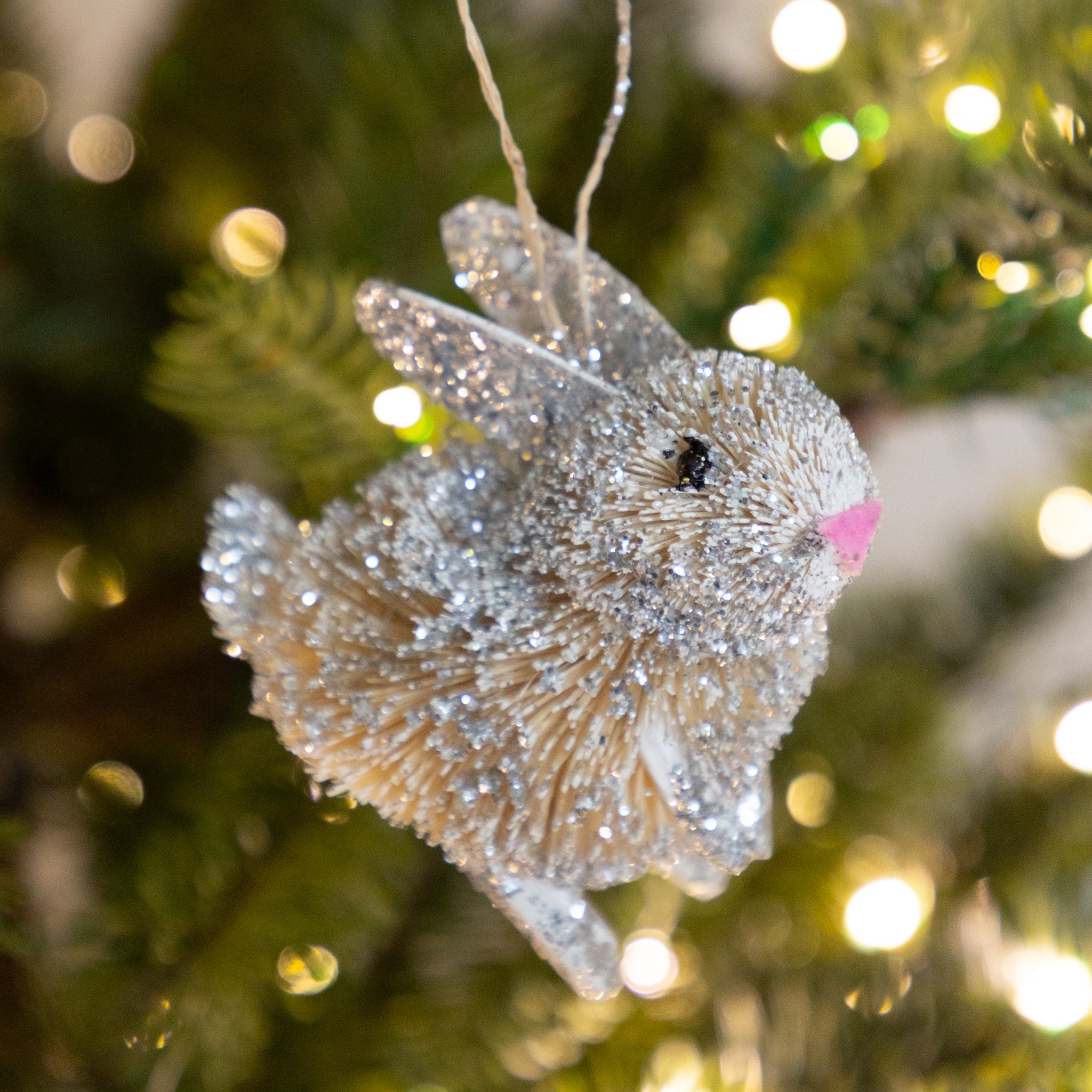 Decorative bunny ornament on a Christmas tree with blurred lights in the background.
