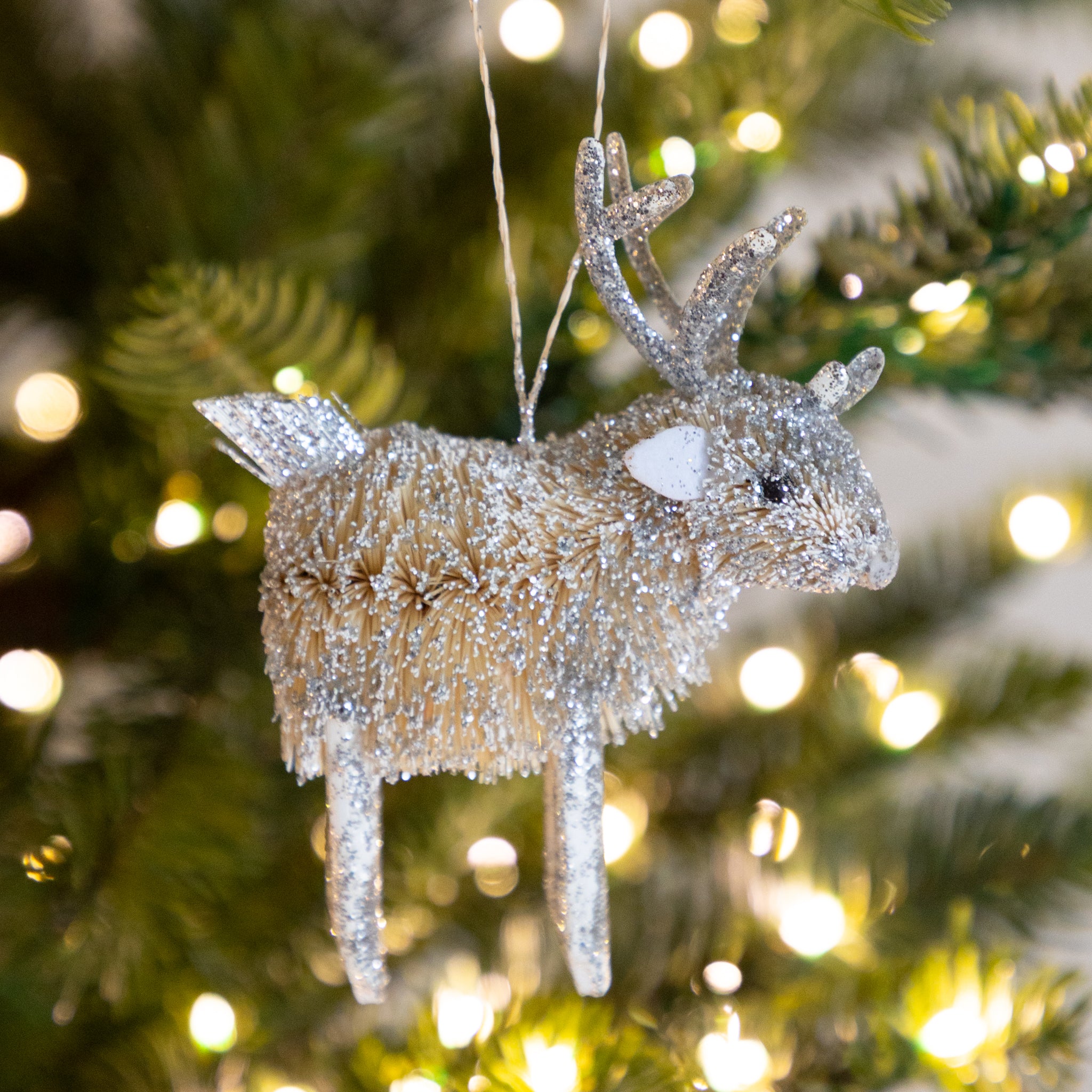 Decorative deer ornament with glittery texture hanging on a Christmas tree.