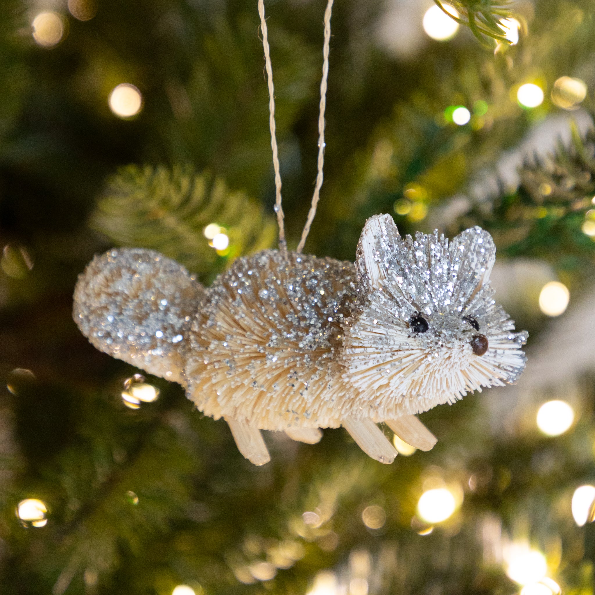 Sparkly fox ornament hanging on a Christmas tree with blurred lights in the background.