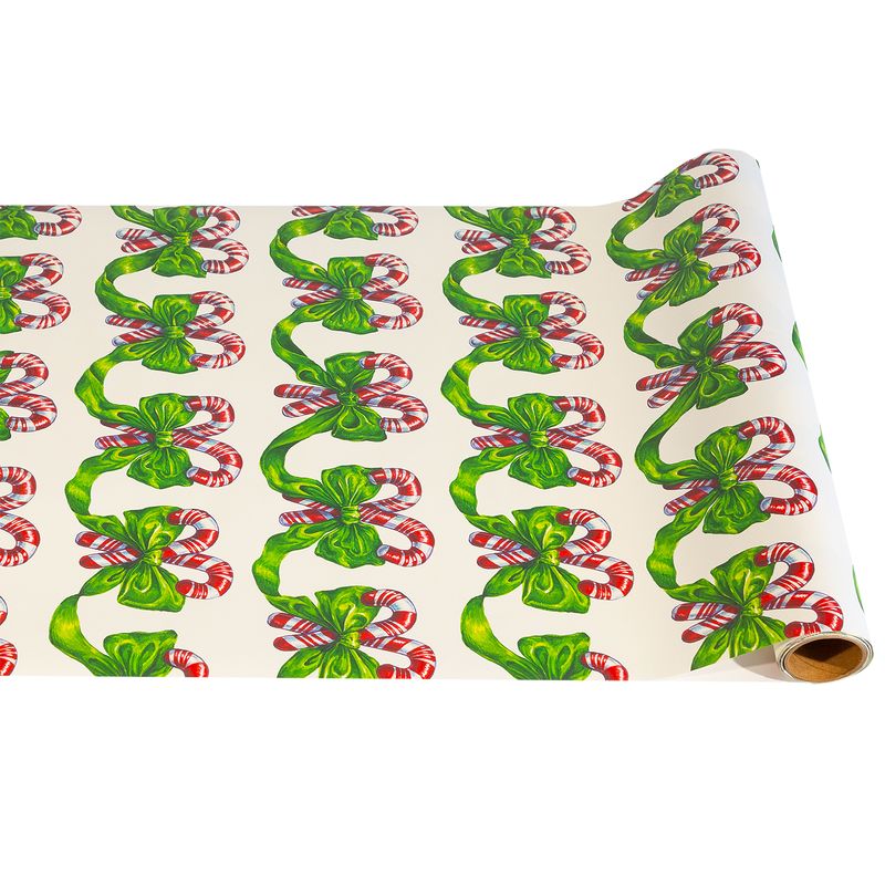 A paper runner roll featuring a repeating illustrated pattern of green ribbon tied in bows around red and white striped candy canes on a cream background. 