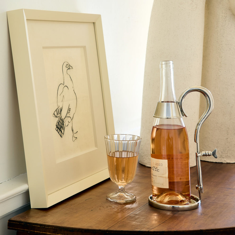 Bottle of rose wine with a glass and a framed drawing on a wooden surface.