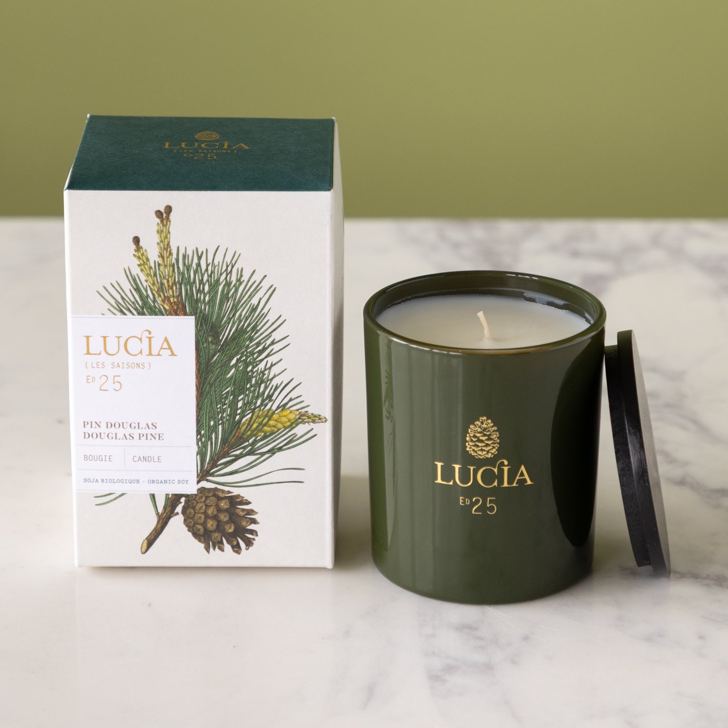 Green Lucia candle with packaging featuring pine branches on a marble surface.