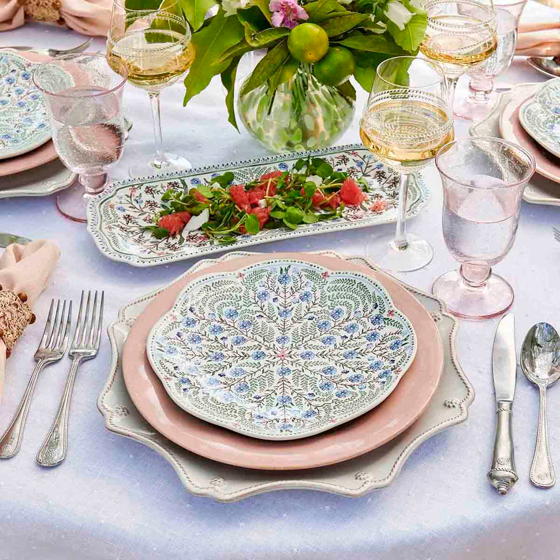 An elegantly set dining table with Juliska Villa Seville dinner plates, silverware, and glasses of wine.