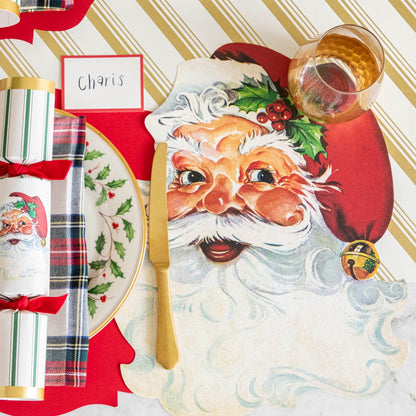 The Gold Peppermint Stripe Runner under an elegant table setting featuring the Die-cut Santa Placemat and Red Frame Place Card with the name &quot;Charis&quot; written on it.