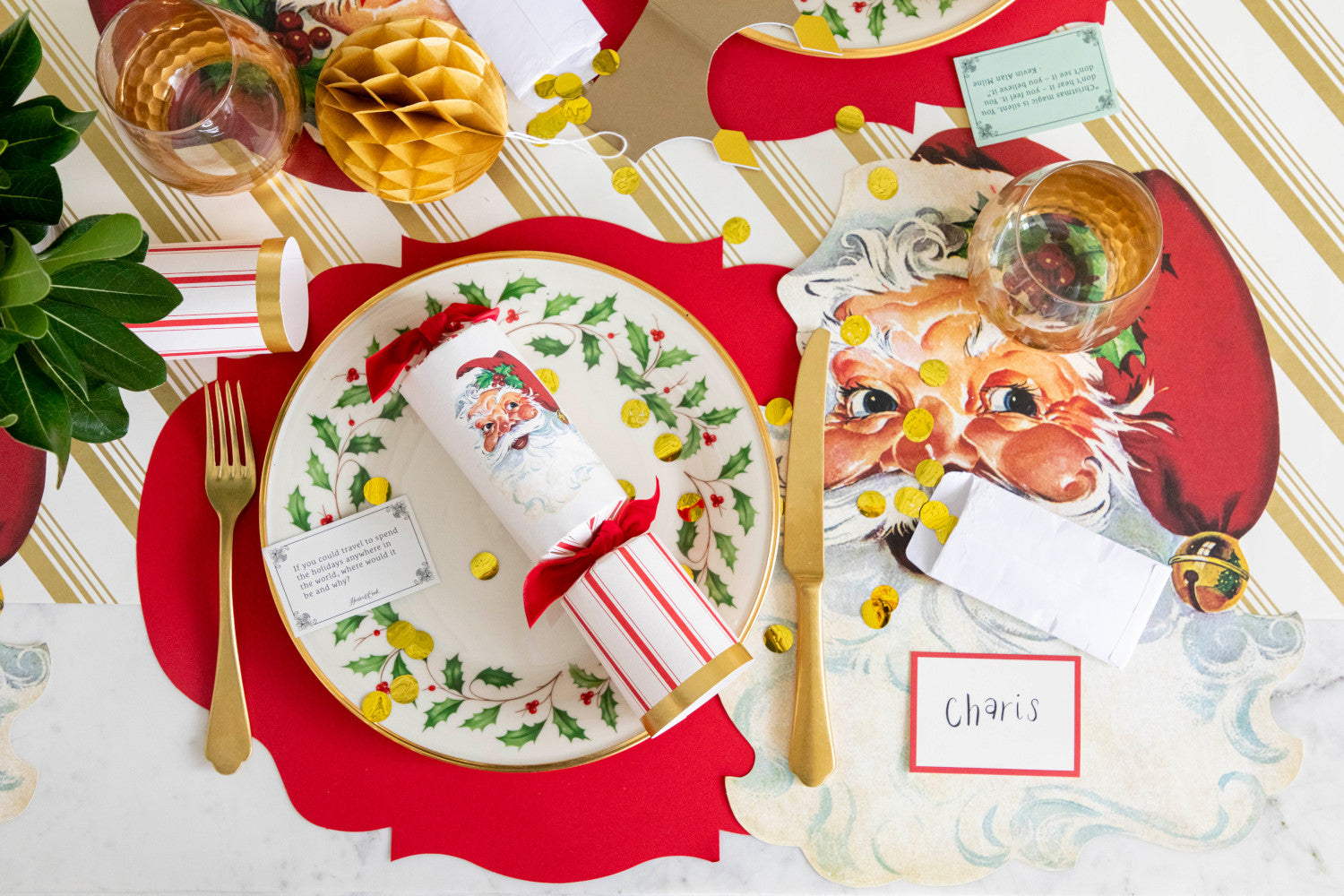 Christmas-themed table setting with Die-cut Santa placemat, Die-cut Red French Frame Placemat and festive dinnerware on the Gold Peppermint Stripe Runner.