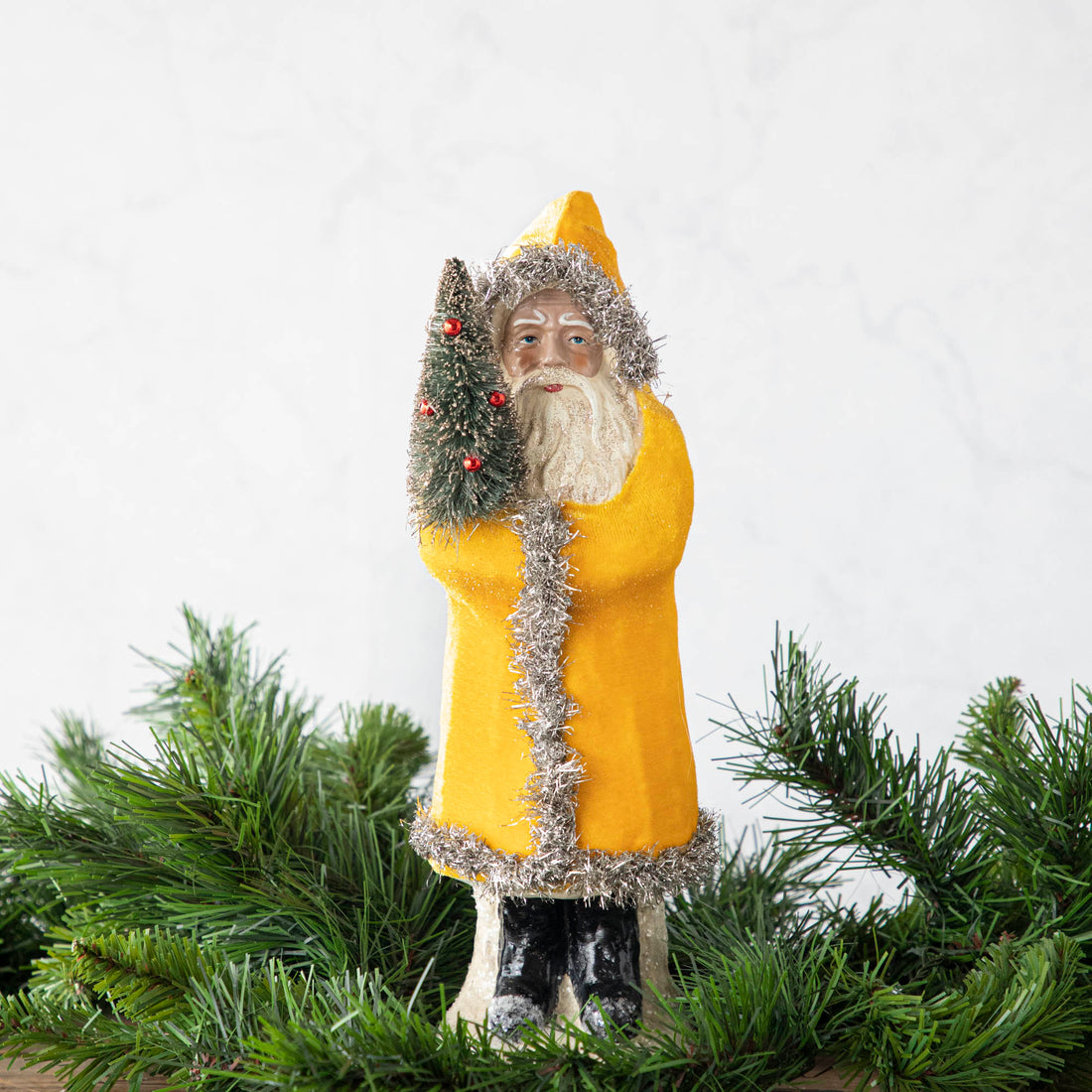 A 12&quot; Velvet Belsnickle figurine with a yellow velvet robe adorned with tinsel trimming and glitter, holding a tree.