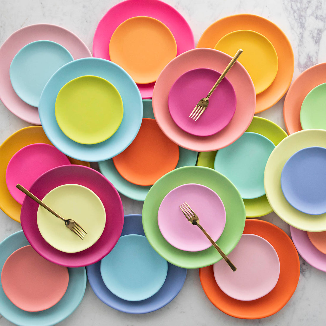 Colorful plates and forks arranged on a marble table.