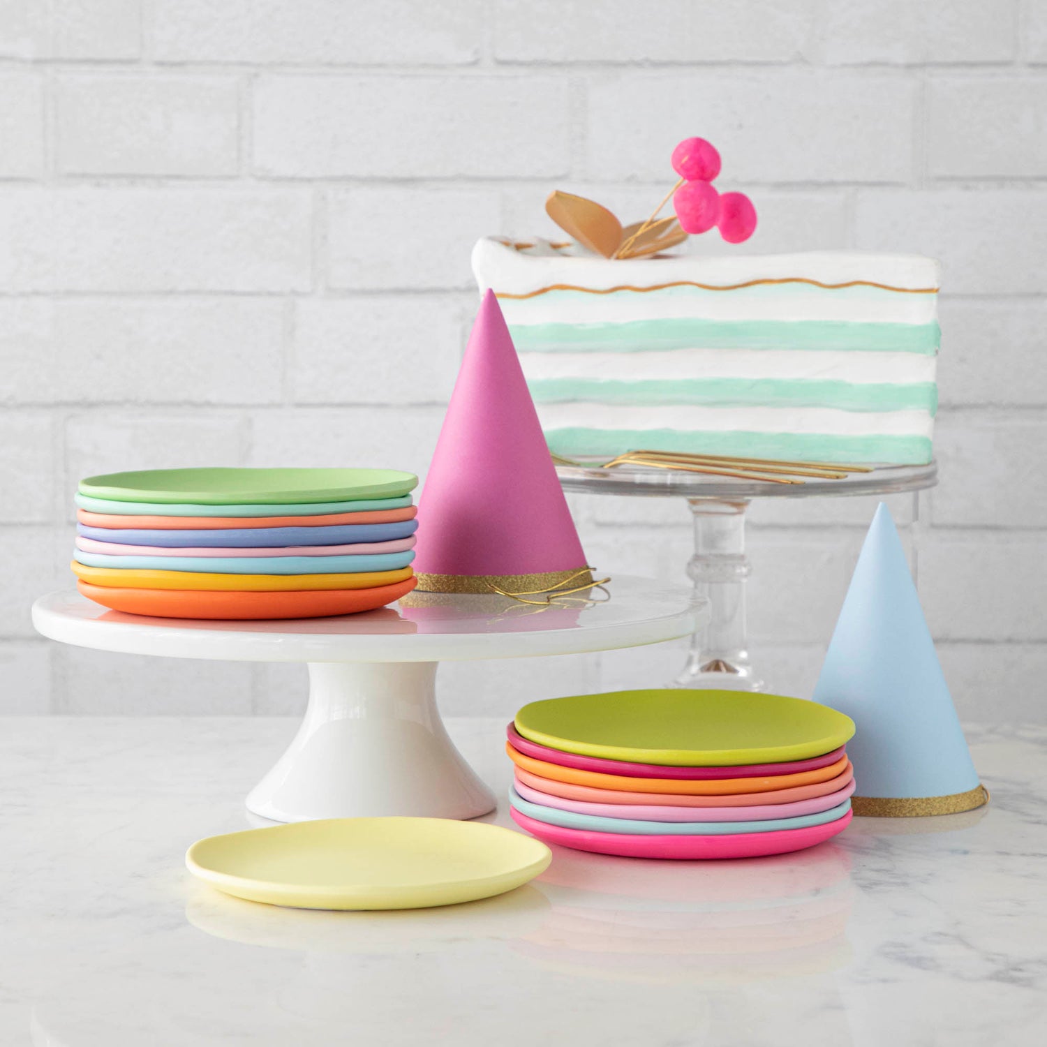 Colorful party hats and rainbow melamine dessert plates on a white table.