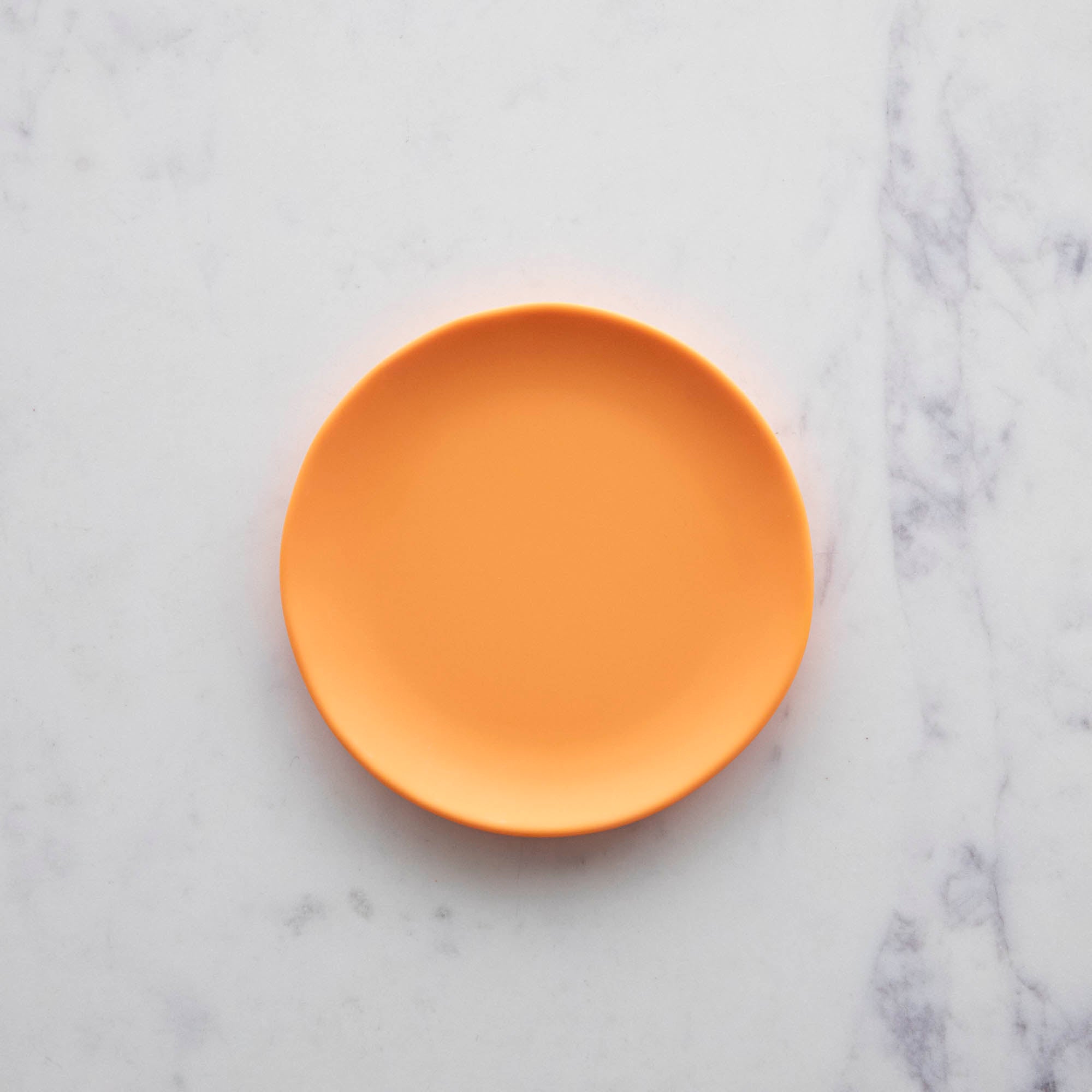 A 6&quot; cantaloupe orange Rainbow Melamine Plate by Glitterville on a marble surface.