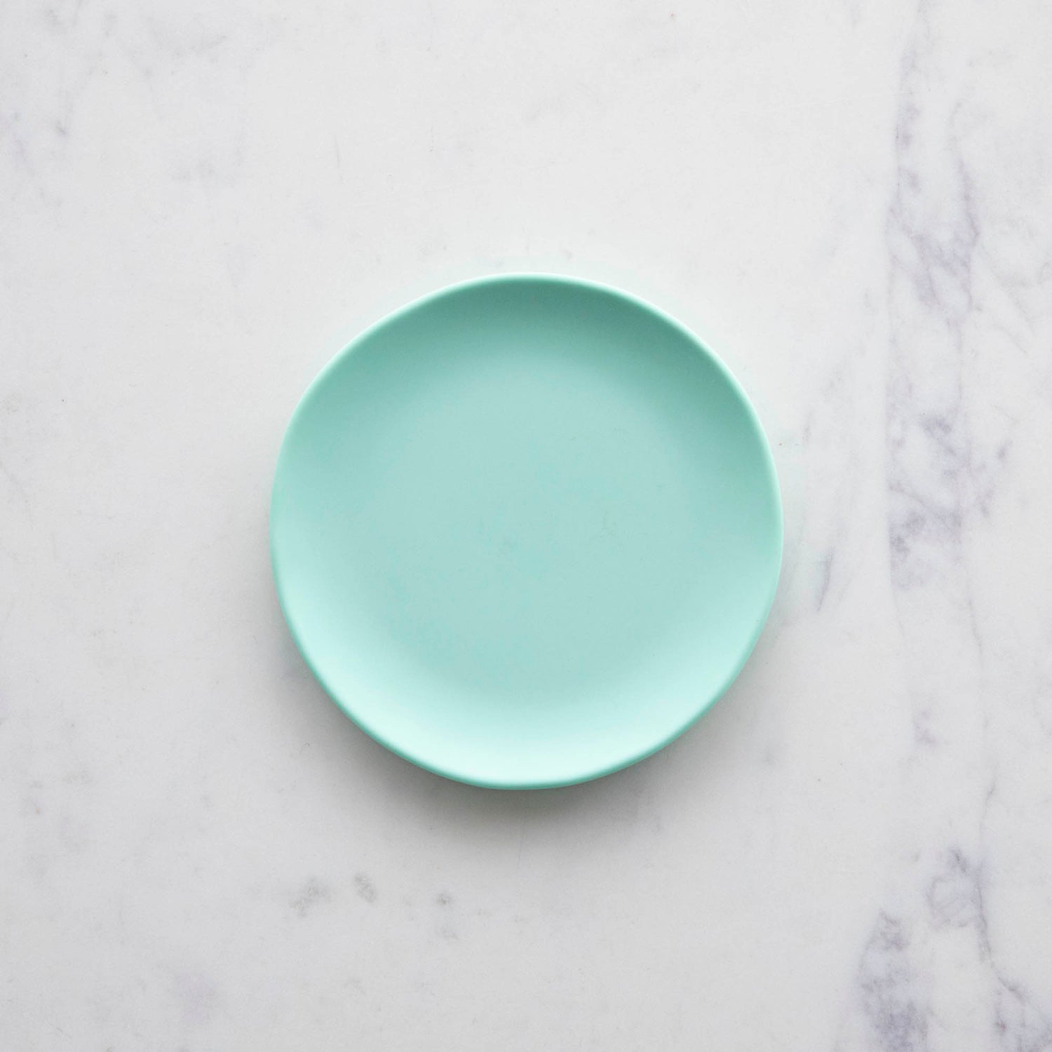 A 6&quot; mint Rainbow Melamine Plate by Glitterville on a marble surface.