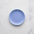 A 6" huckleberry blue Rainbow Melamine Plate from Glitterville on a marble surface.