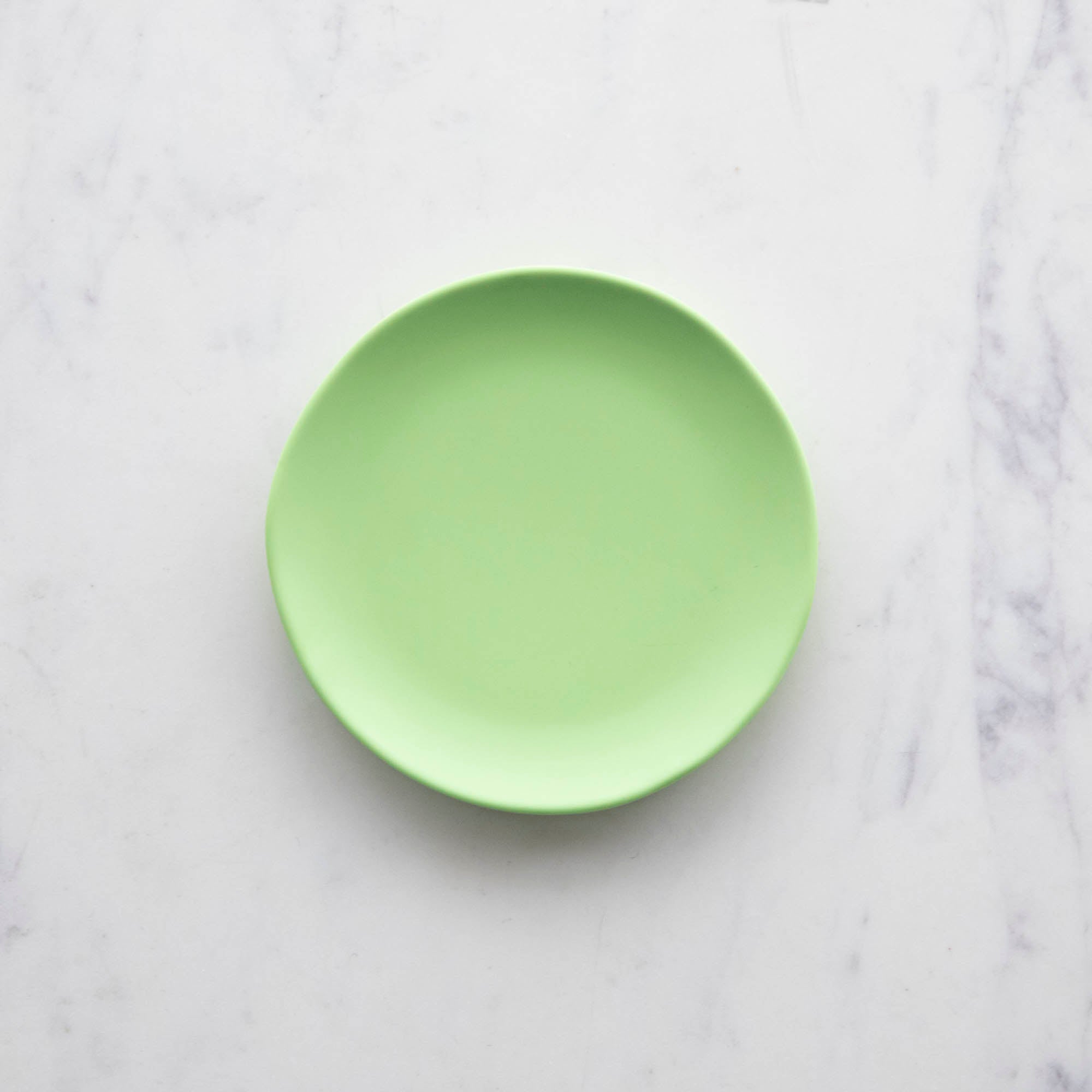A 6&quot; Lime Rainbow Melamine Plate by Glitterville on a marble surface.