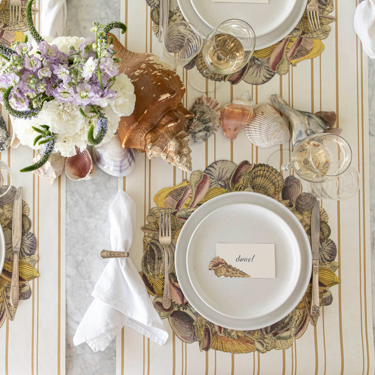Die-cut Shell Wreath Placemat under an elegant place setting, on the Antique Gold Stripe Runner.