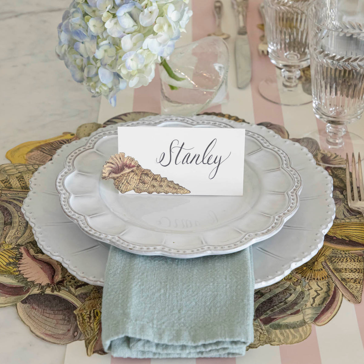 Die-cut Shell Wreath Placemat under a place setting on a shell themed table.