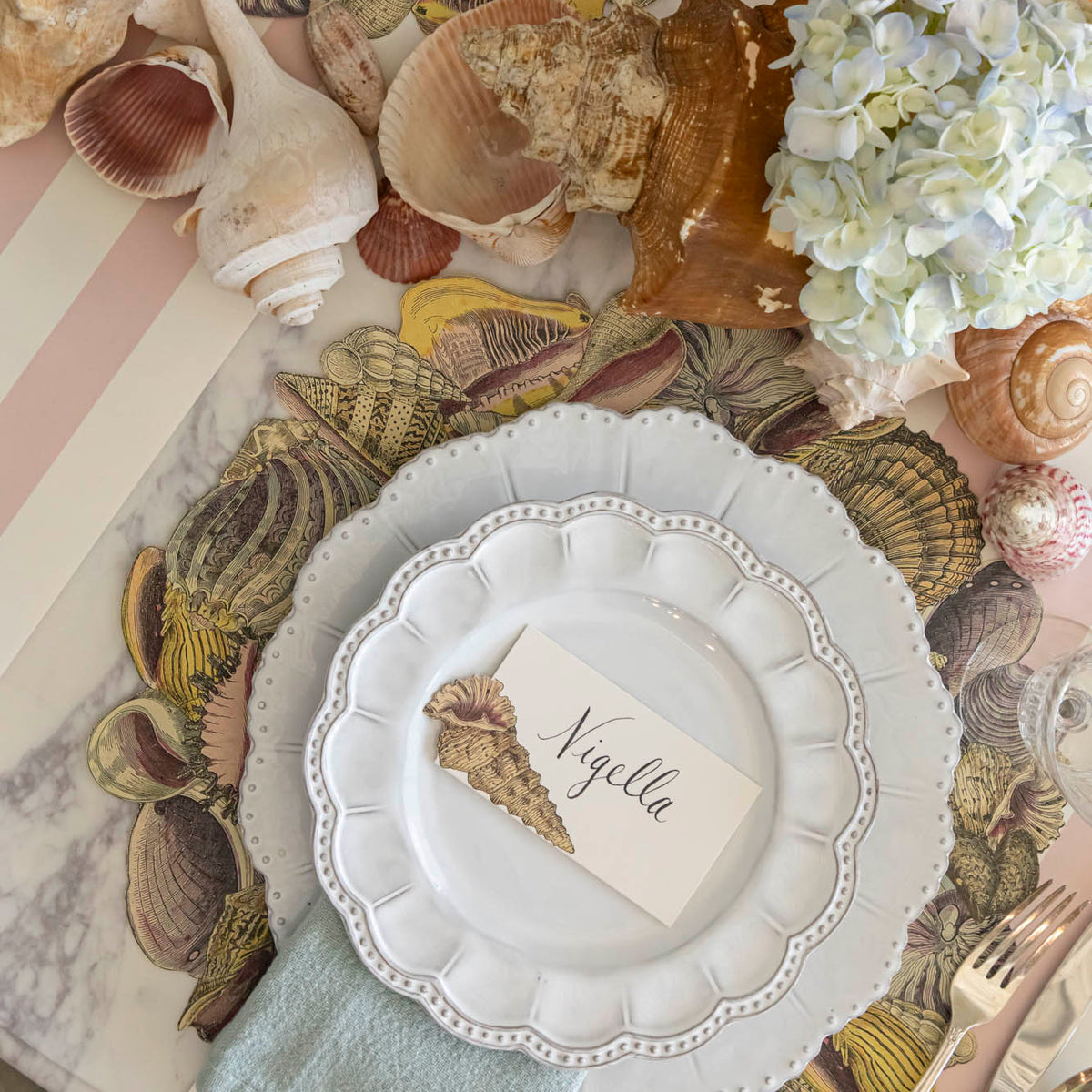 Die-cut Shell Wreath Placemat under a place setting on a shell themed table.