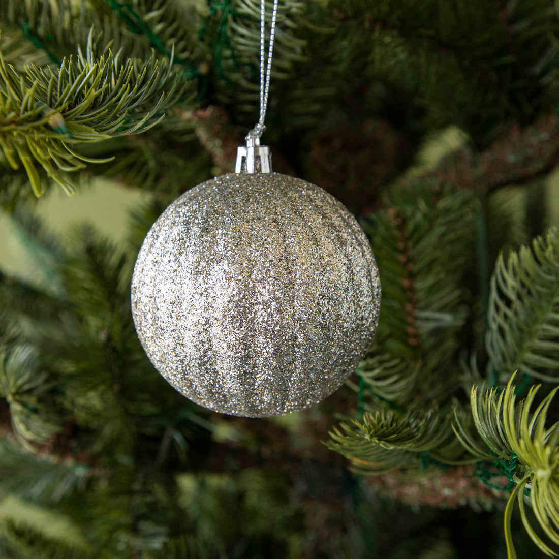 Round silver glitter ornament hanging on a tree.