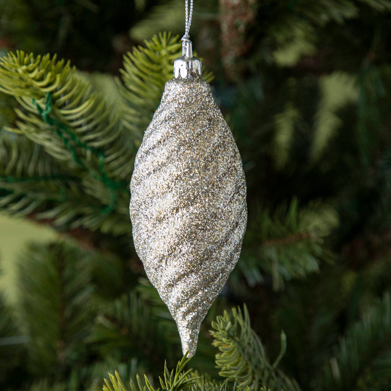 Drop shape silver glitter ornament hanging on a tree.