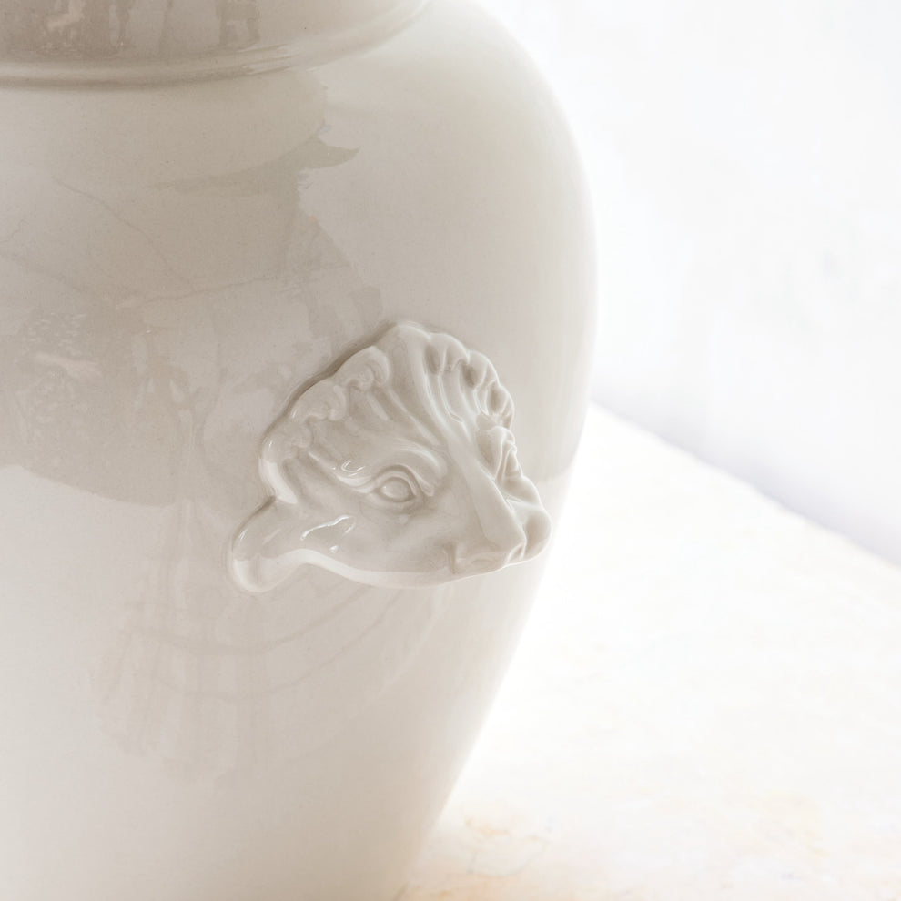 Close-up of a white ceramic vase with a face design on a light background.