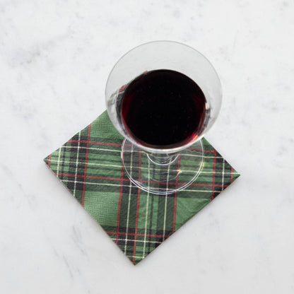 A square cocktail napkin featuring a diagonal plaid pattern of black, red and white over medium green.