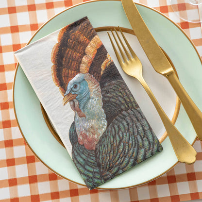 A Heritage Turkey Guest Napkin on a plate in an elegant Thanksgiving place setting.