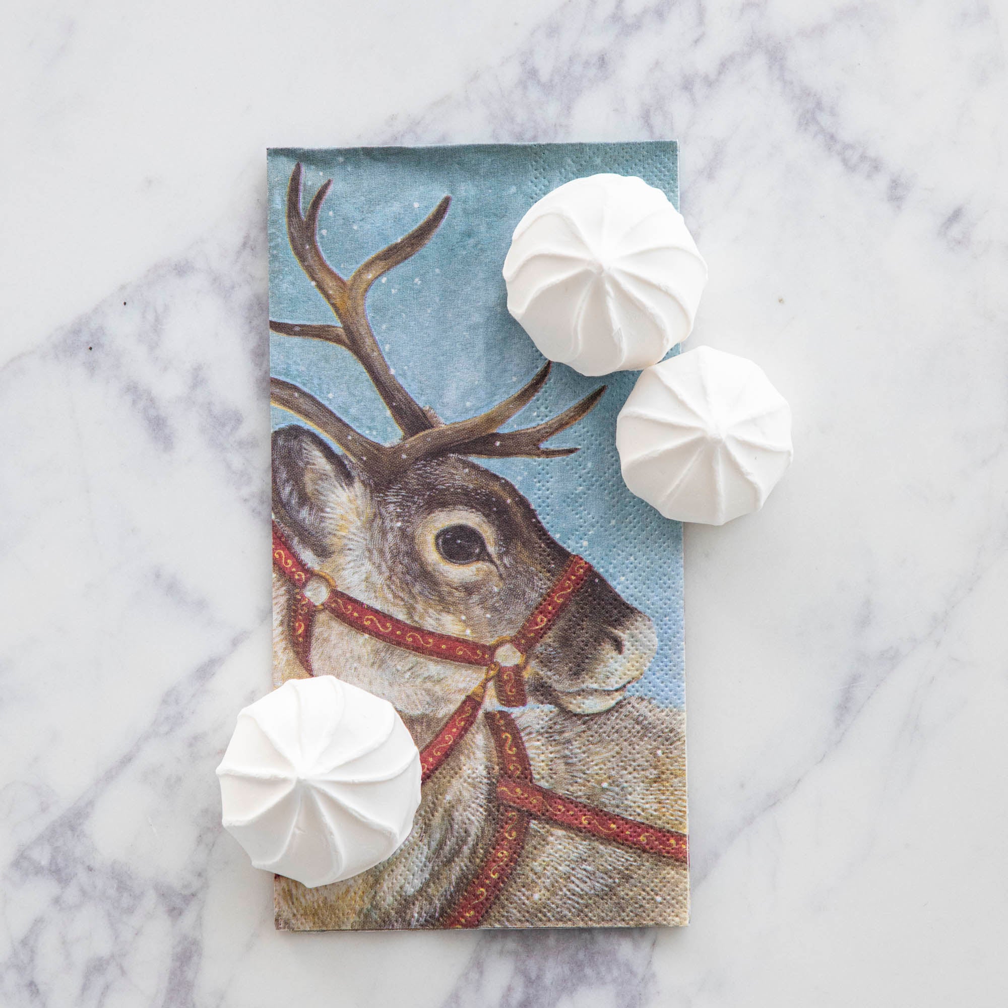 A Dashing Reindeer Guest Napkin under three white marshmallow puff treats.