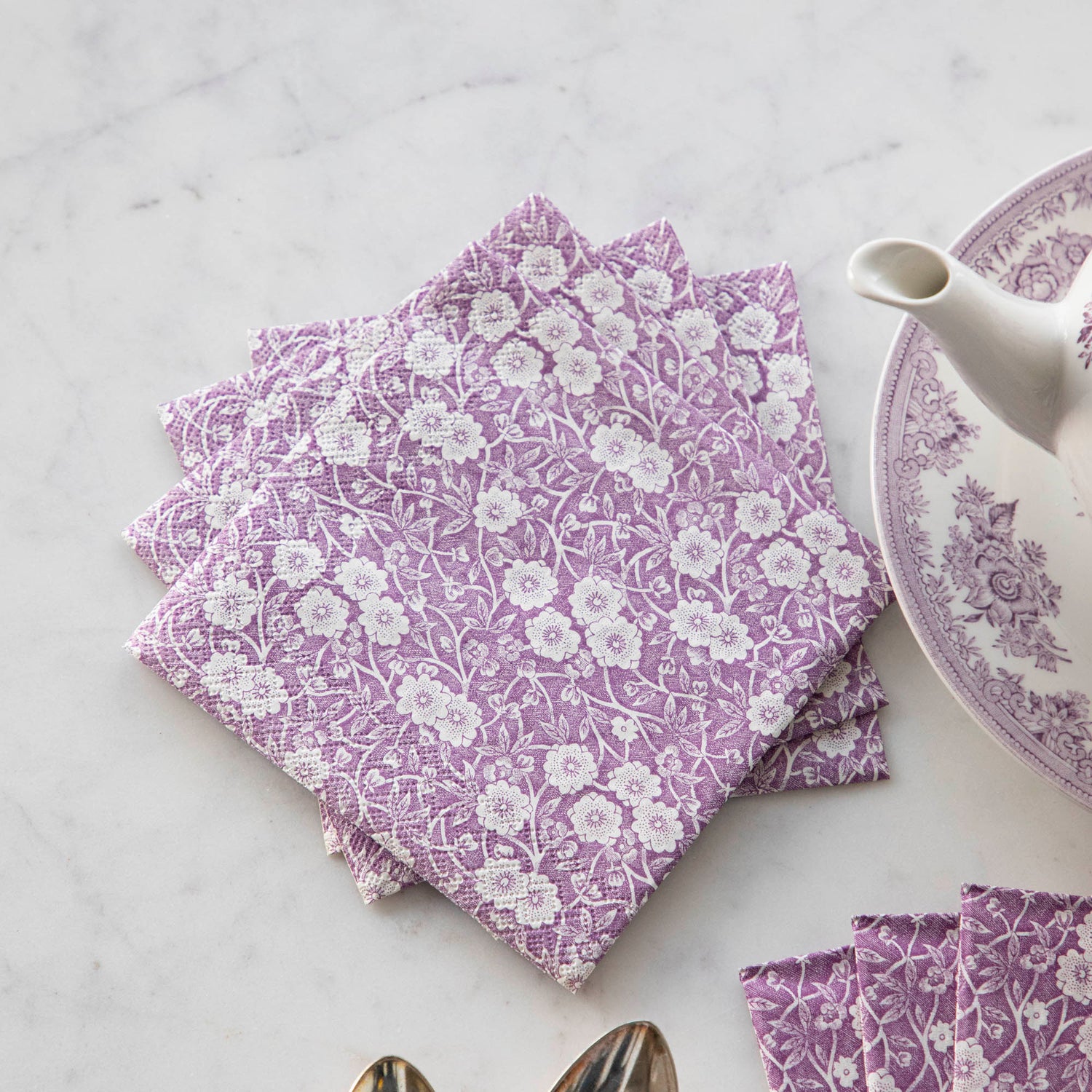 A set of beautiful Lilac Calico Napkins by Hester &amp; Cook exquisitely decorated on a table next to a teapot.