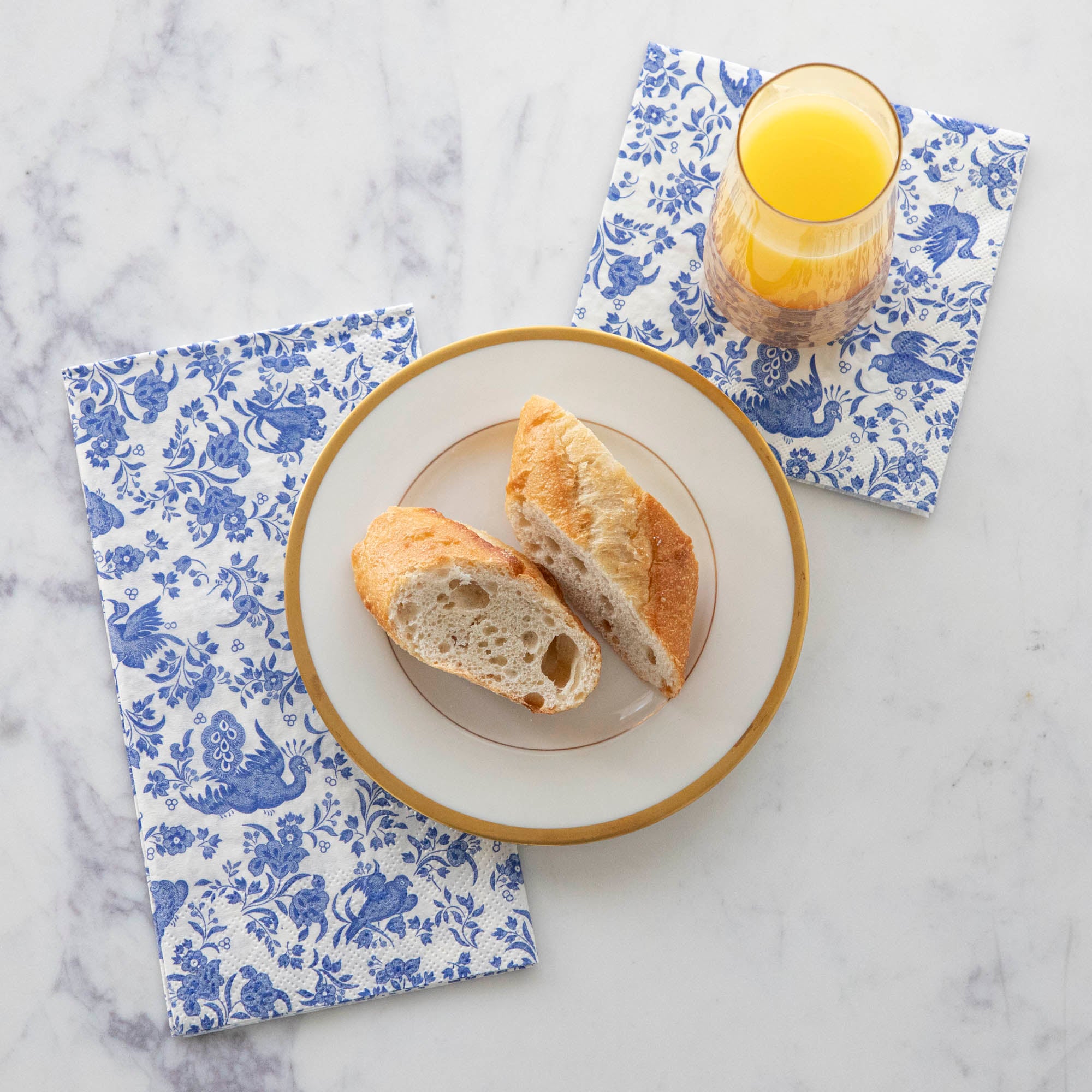 A plate of bread and a glass of juice with Blue Regal Peacock Napkins by Hester &amp; Cook.