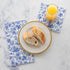 A plate of bread and a glass of juice on top of Blue Regal Peacock Guest and Cocktail Napkins by Hester & Cook.